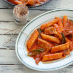 Spicy Korean rice cakes (tteokbokki) is made with gochujang and served on a platter with toothpicks.