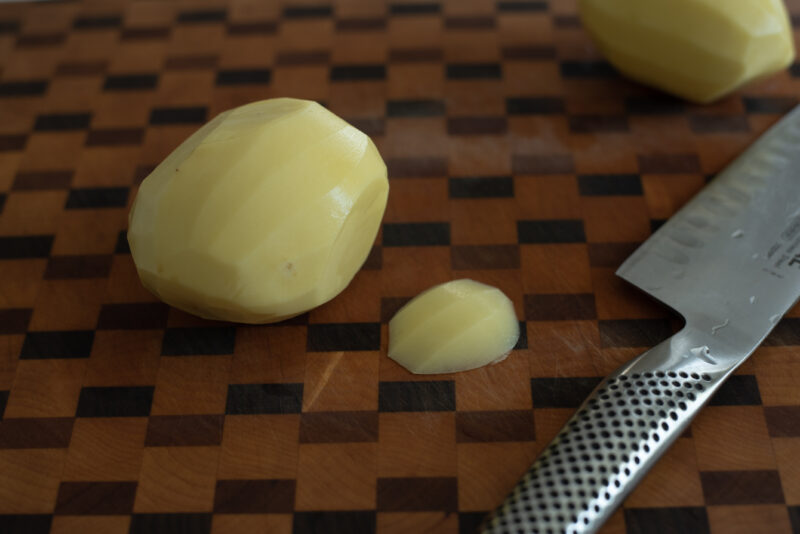 A small slice of potato is cut off from the bottom with a knife to create a flat surface.