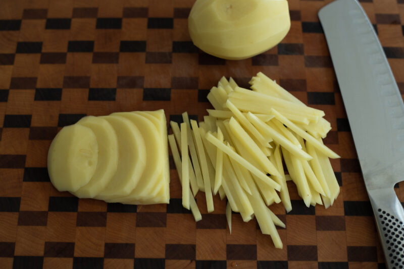 Thin slices of potato is cut into thin matchsticks with a knife on the cutting board.
