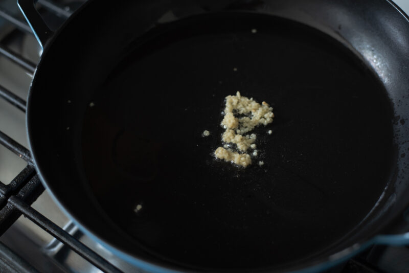 A small amount of minced garlic is added to hot oil in a skillet.