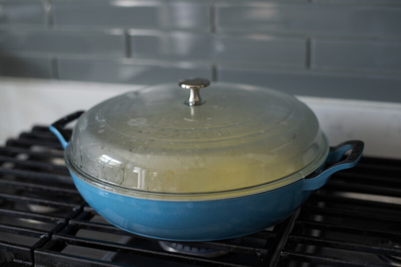 A glass dome lid is covering the pan over the stove.
