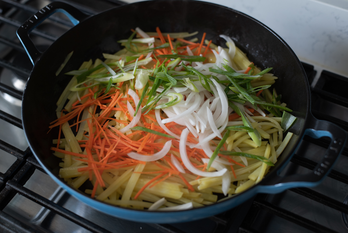 Onion, carrot, green onion slices are added to pan-fried potatoes.