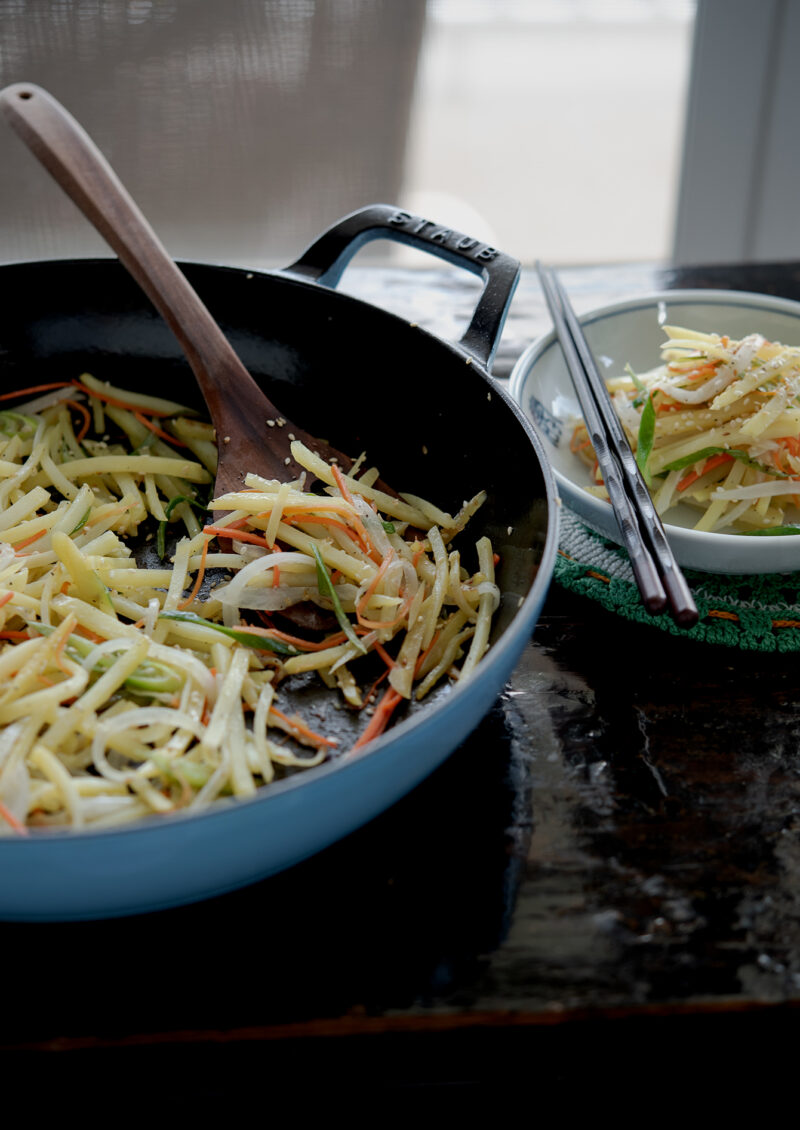 pan-fried potato and vegetable are dished into a small serving plate with chopsticks.