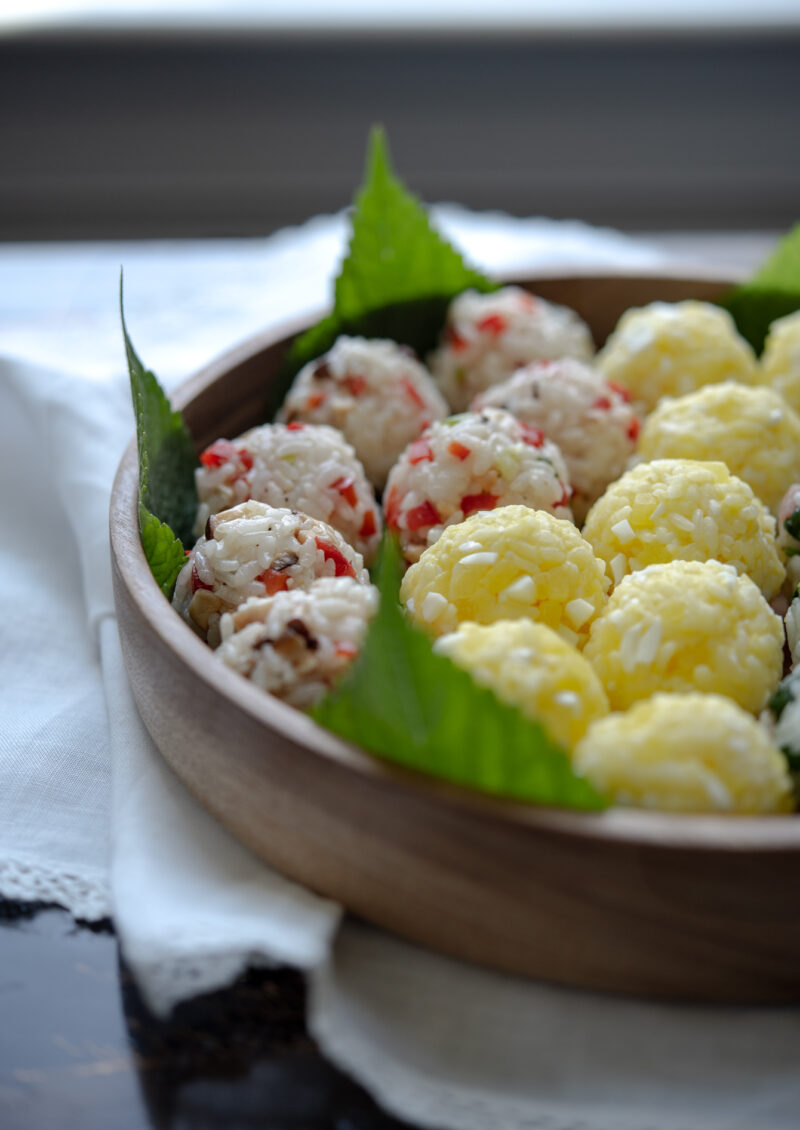Korean rice balls arranged in a wooden serving bowl lined with perilla leaves.
