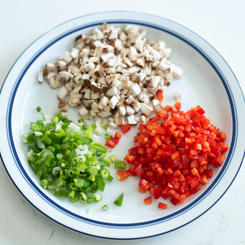 Minced mushroom, red pepper, and green onion are placed on a plate.