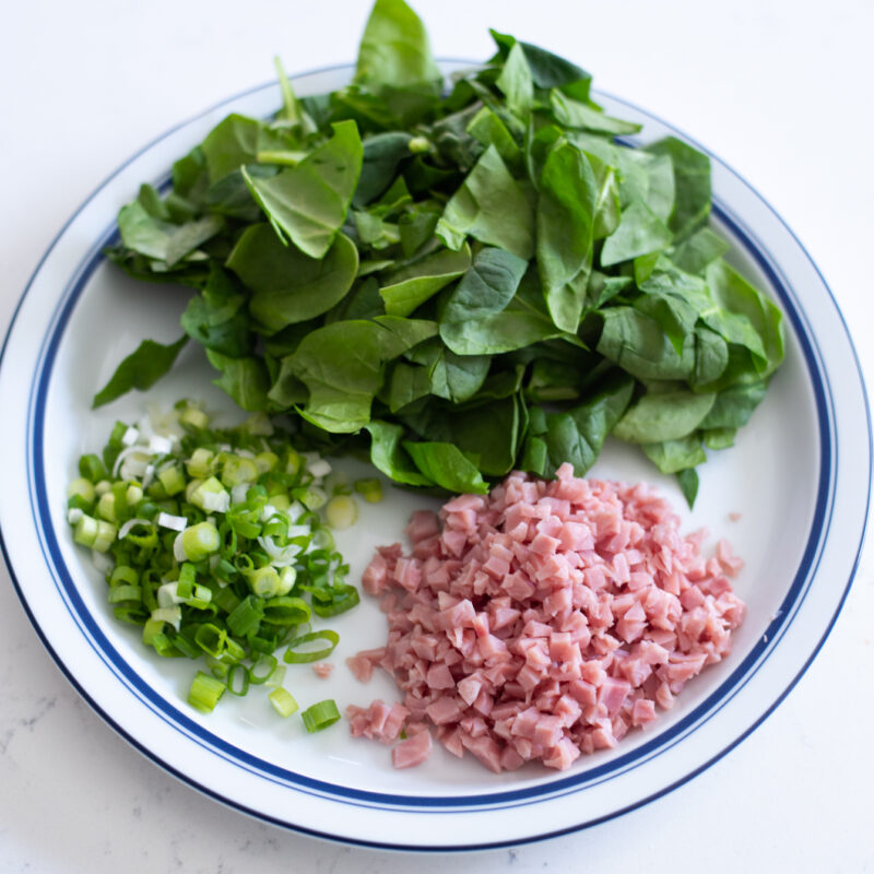 Chopped spinach, ham, and green onion are placed on a plate.