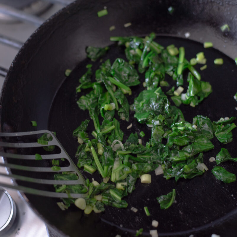 Spinach is cooked with green onion with a little oil in a skillet.