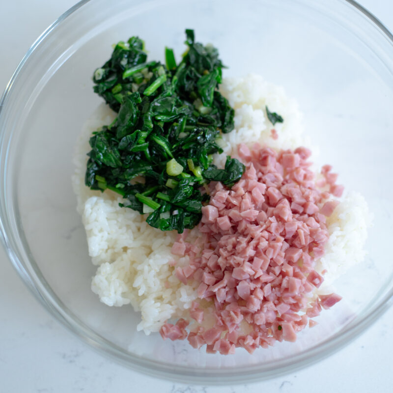 Cooked rice, wilted spinach, chopped ham are combined in a mixing bowl.