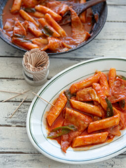 Spicy Korean rice cakes (tteokbokki) is made with gochujang and served on a platter with toothpicks.