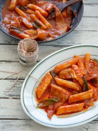 Spicy Korean rice cakes (tteokbokki) is made with gochujang and served on a platter with toothpicks.