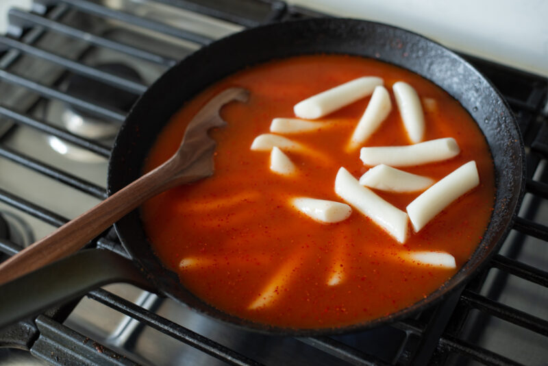 Tteokbokki sauce and anchovy stock added to rice cakes in a skillet