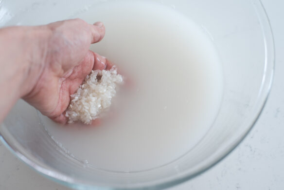 A hand is swirling the rice in water.