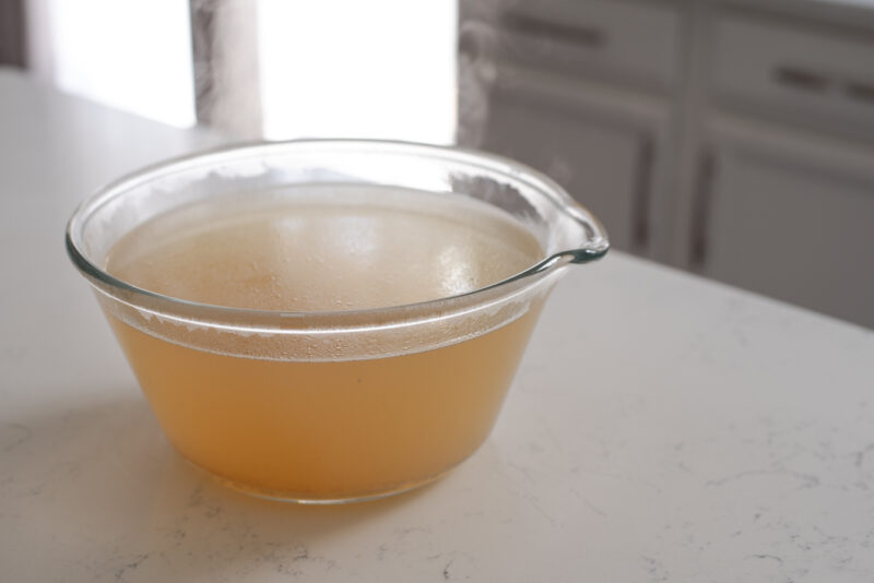 Flavorful beef stock is cooling in a large glass bowl.