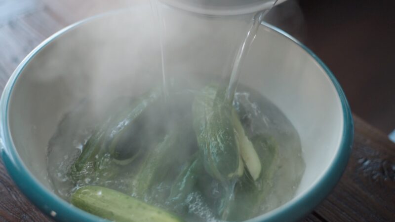 Pour salted boiling water poured into a bowl with cucumbers.