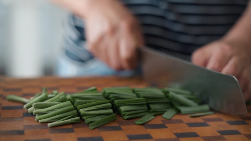 Asian chives are sliced with a knfie.
