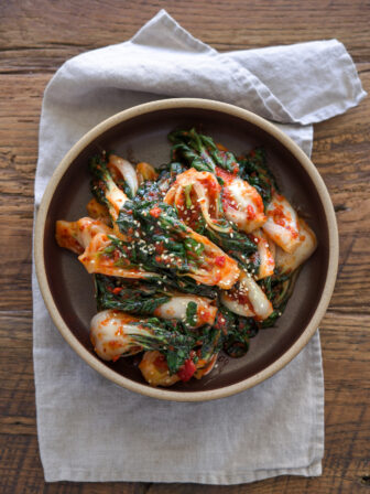 Bok choy kimchi made with fresh chili shows its vibrant red color in a bowl.