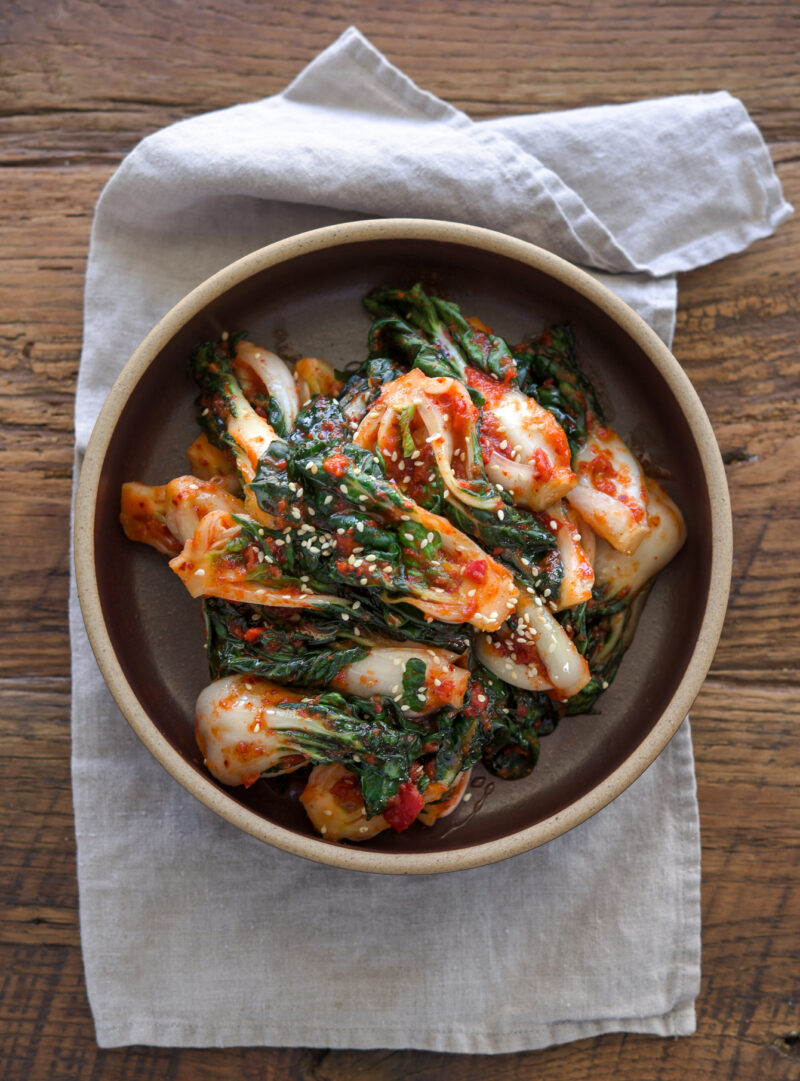 Bok choy kimchi made with fresh chili shows its vibrant red color in a bowl.
