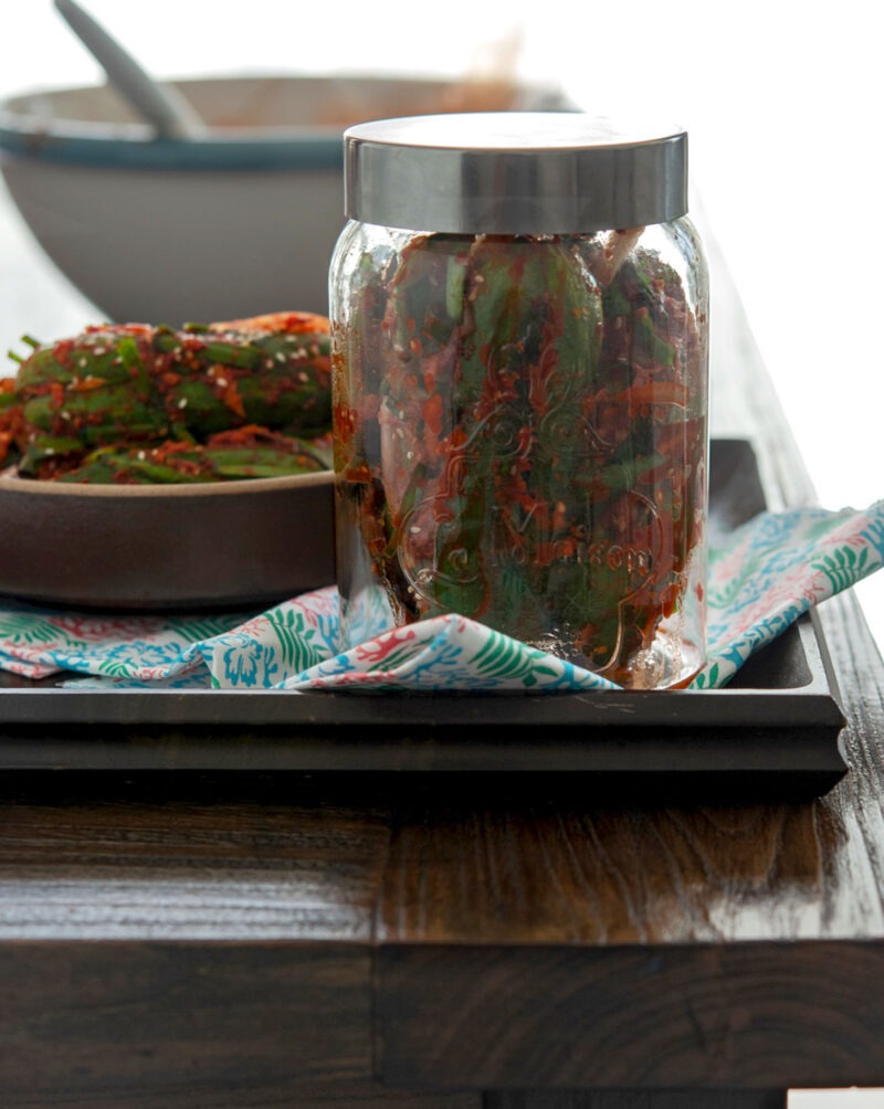 Cucumber kimchi (oi sobagi) fermenting in a glass jar beside freshly made stuffed cucumber kimchi