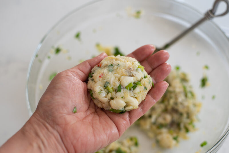 A hand is forming a crab cake patty on the palm.