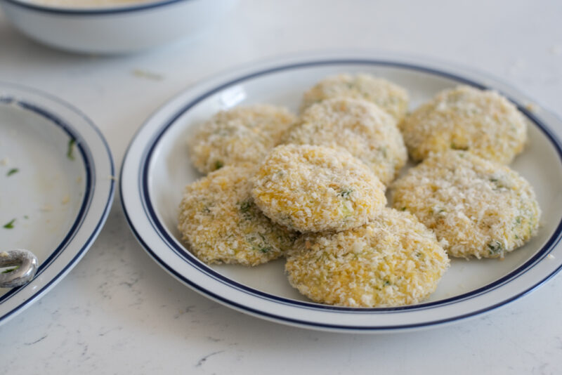 Crab cake patties are coated with breadcrumbs and placed on a plate.