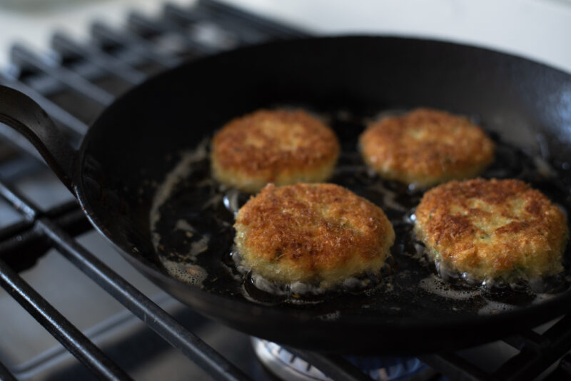 Thai crab cakes are pan fried to golden crisp in a skillet on the stove.