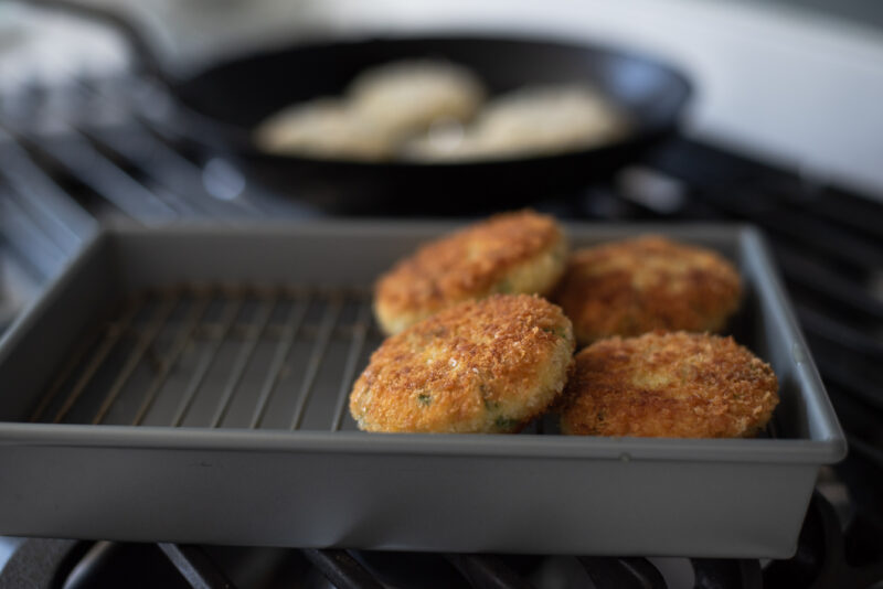 4 pieces of crispy pan fried crab cakes are sitting on a wired rack.