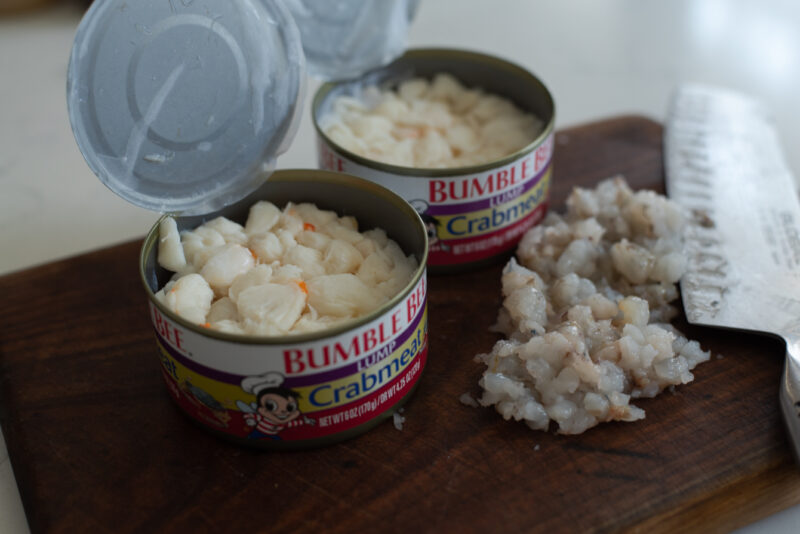 Two cans of crabmeat are opened and placed next to minced shrimp.