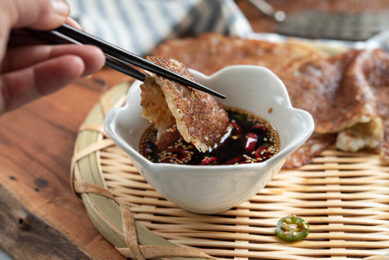 Chopsticks are used to dip the crispy Korean potato pancakes in a soy chili dipping sauce.
