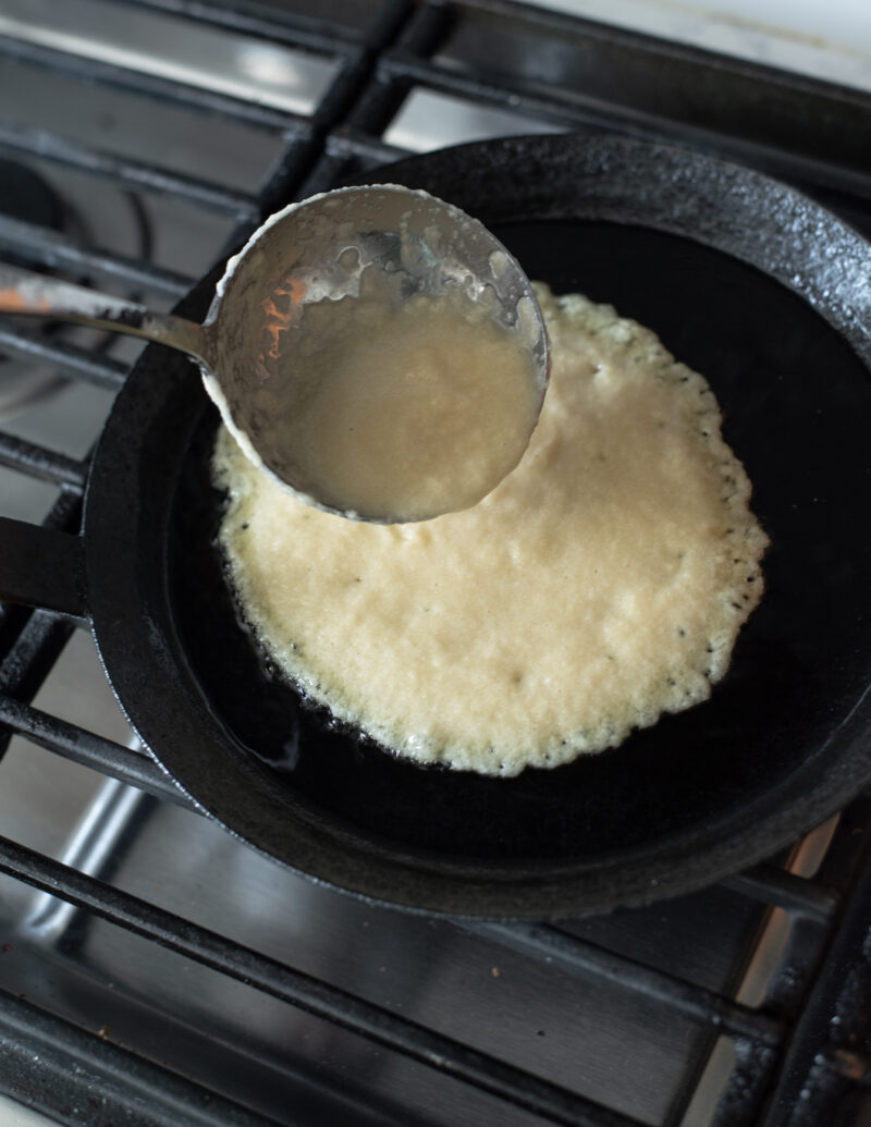 A ladle is pouring potato pancake batter to a skillet over the stove.