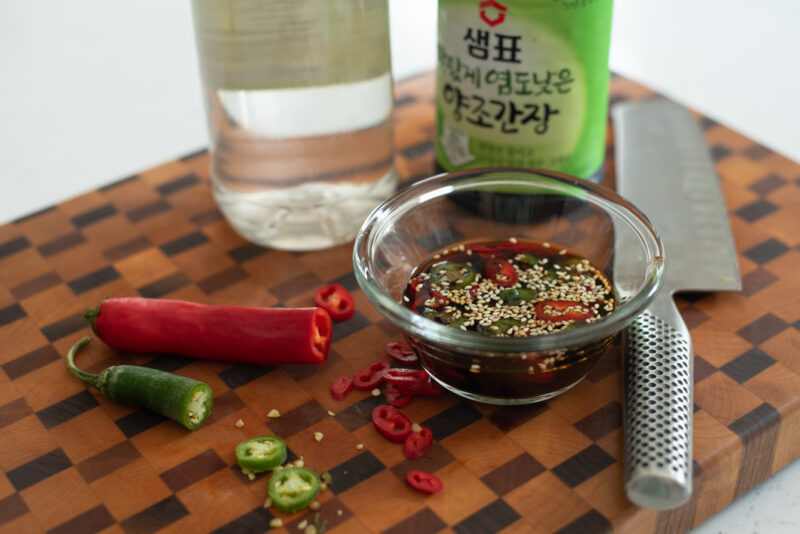 Green and red chili are chopped and added to a sauce mixture in a small bowl.