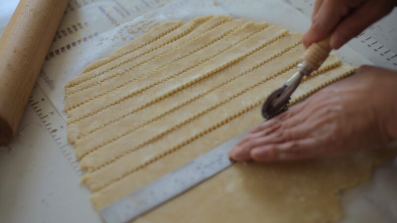 A roller cutter is cutting the fluted strips for top pie crust.