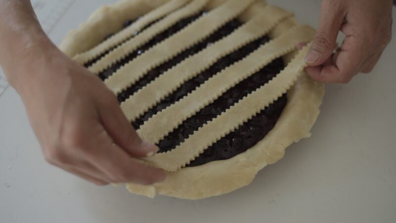 Fluted pie crust strips are laid on top of blueberry pie filling.