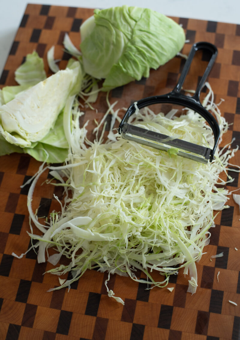 Green cabbage is shredded with a vegetable peeler.