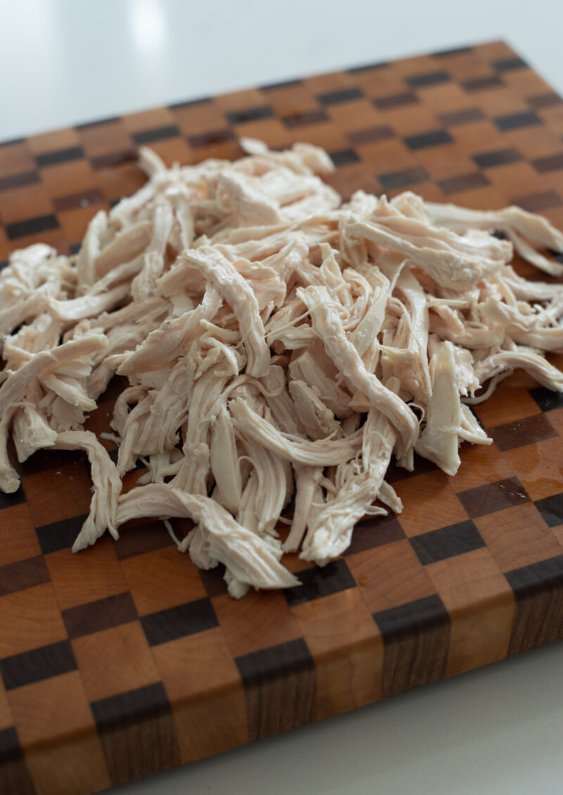 Poached chicken breasts are being shredded on a cutting board.