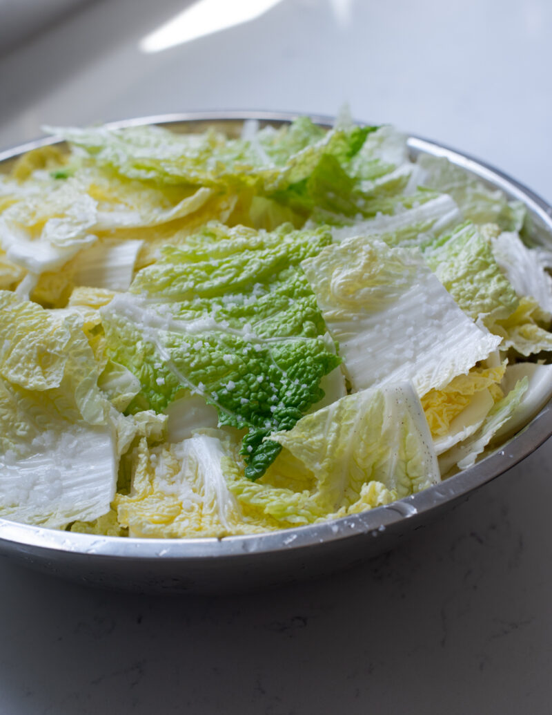 Cabbage pieces are sprinkled with coarse sea salt in a large mixing bowl