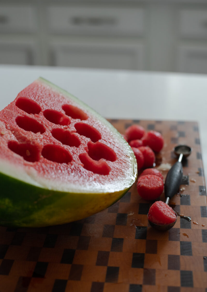 A melon baller is spooning out of watermelon.