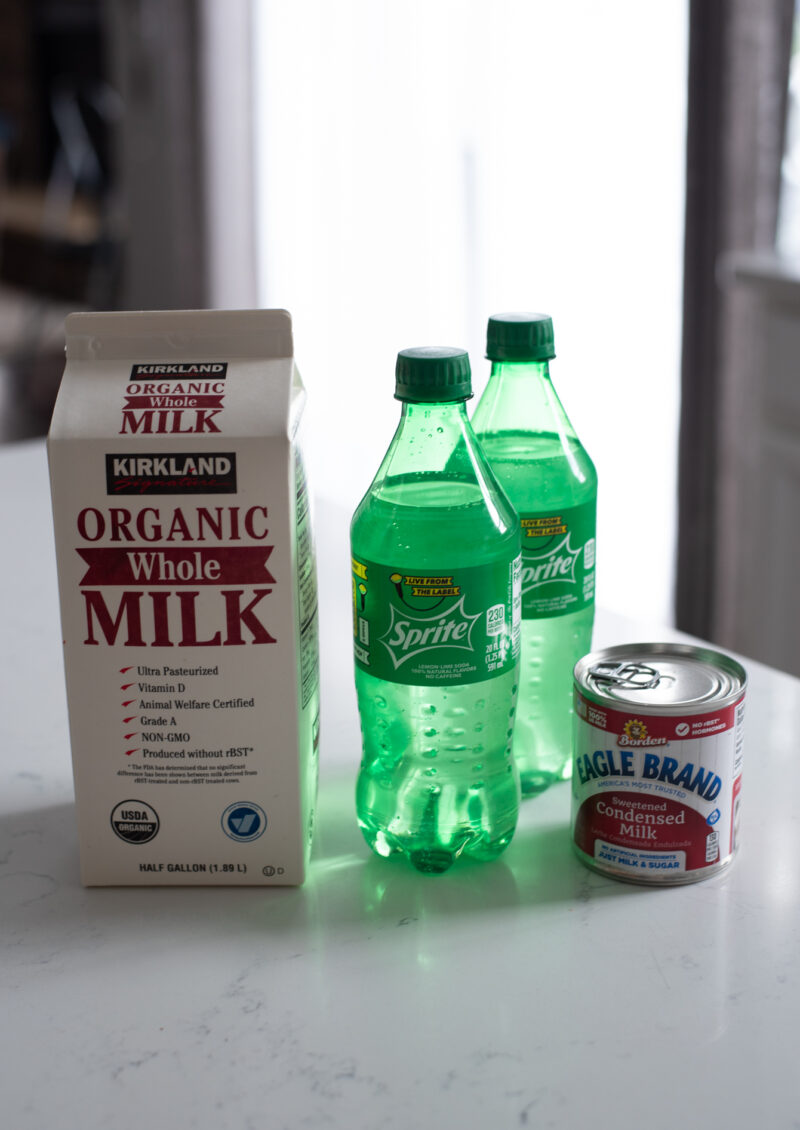 A carton of milk, two sprite bottles, and a can of condensed milk are on the counter.