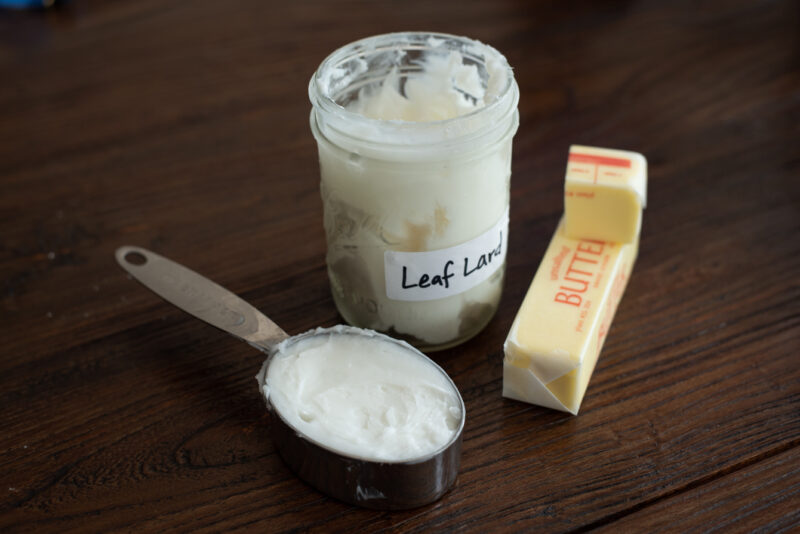 A measuring cup filled with lard and butter sticks are shown on the counter.