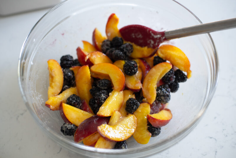 Nectarine slices and blackberries are coated with starch mixture in a bowl.