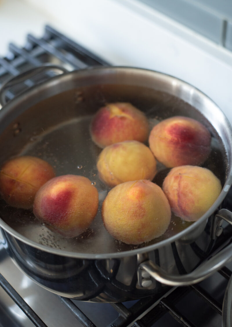 Whole peaches are blanching in the pot of boiling water.