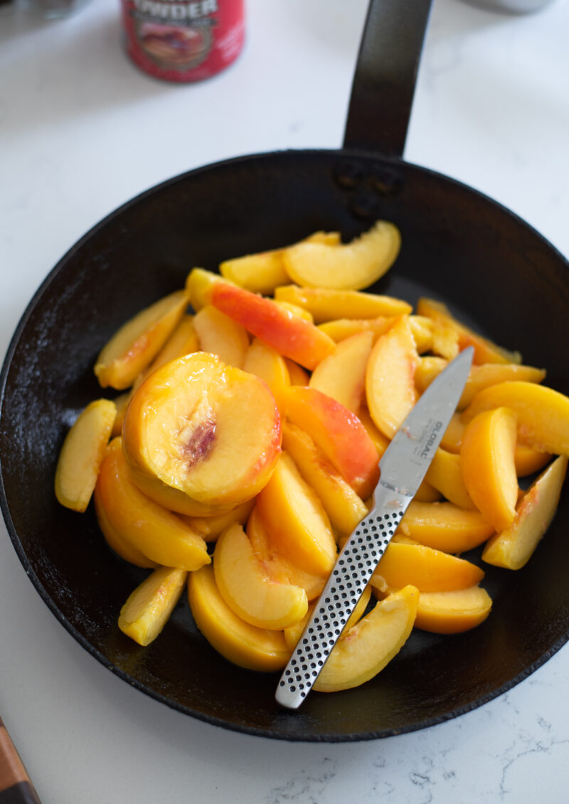 Sliced peaches placed in a skillet to make old fashioned peach cobbler.