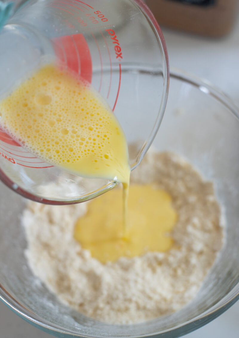egg mixture is being poured on coarse flour crumb mixture in a bowl.