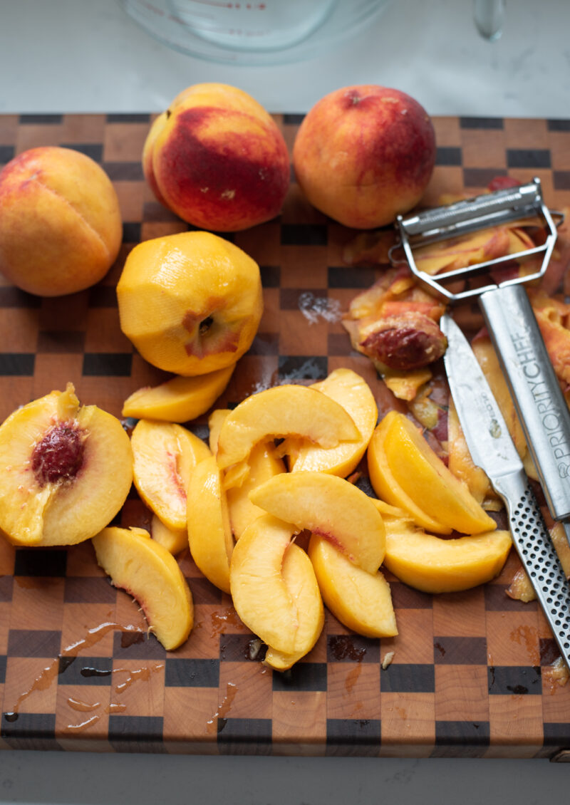 Peeled peaches are pitted and sliced with a pairing knife