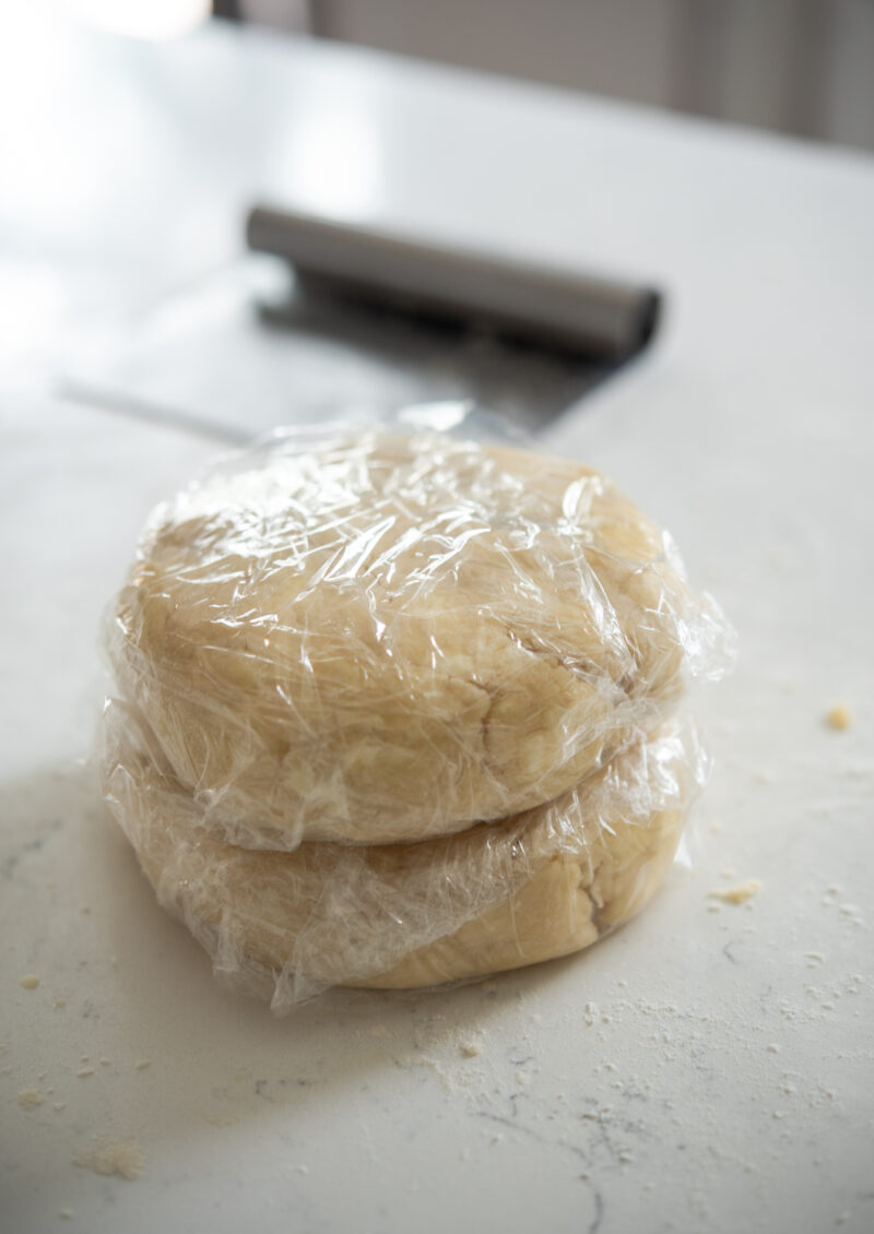 Two pie dough disk is wrapped in plastic and stacked together.