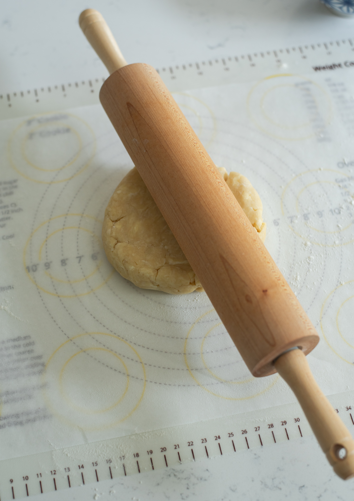 A rolling pin is starting to roll out the firm pie dough on the baking mat.