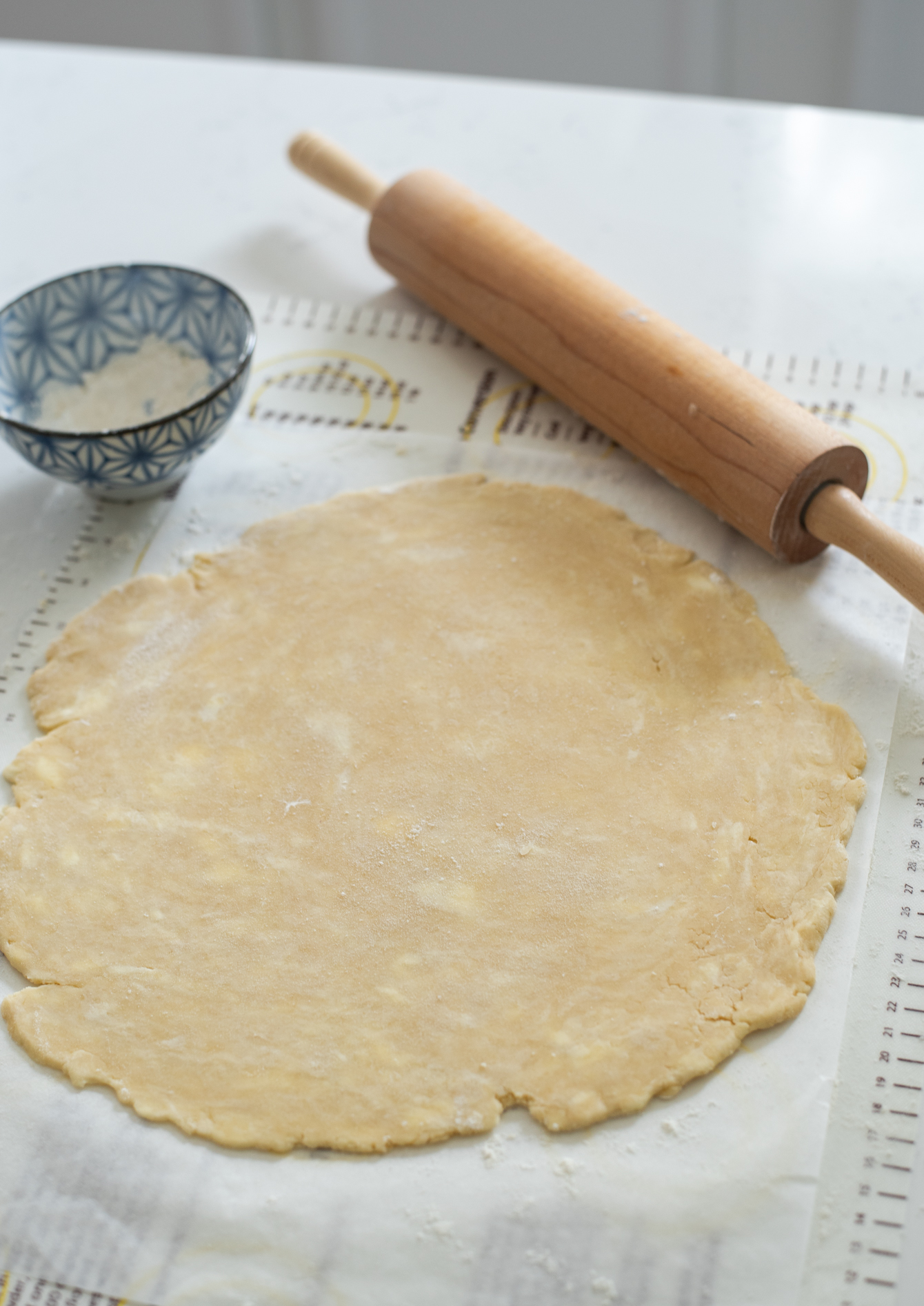 Pie crust is rolled out with a rolling pin on the silicon baking mat