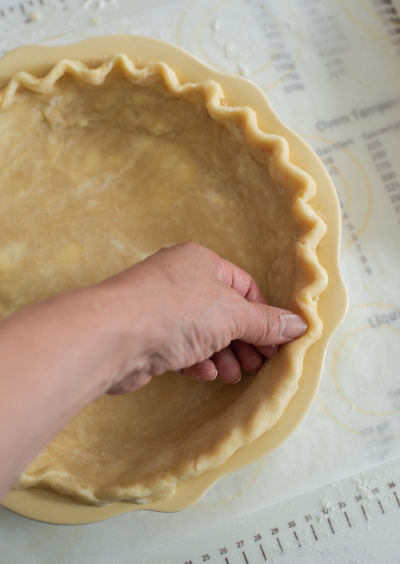 The edge of pie crust on the pie pan is fluted with a finger