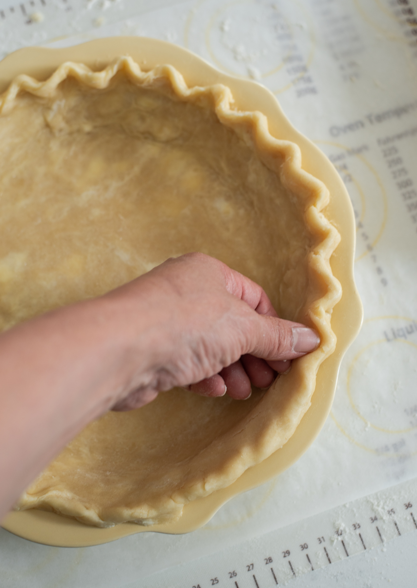 Finger is crimping pie crust into a fluted edge on the rim of pie pan.