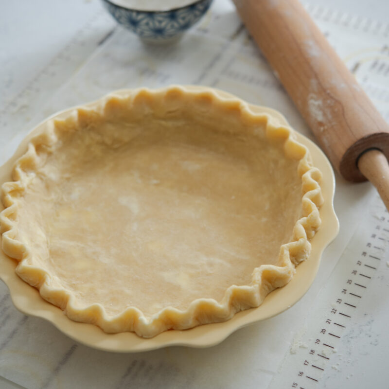 The lard and butter pie crust is rolled and fluted in a yellow pie pan.