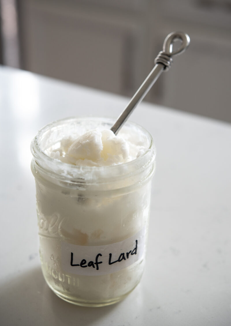A spoon is scooping the leaf lard in a glass container.